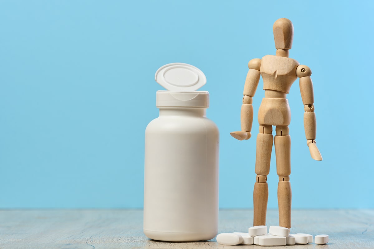 a woody dummy with a plastic bottle and oval white pills on a table, highlighting the withdrawal symptoms of gabapentin