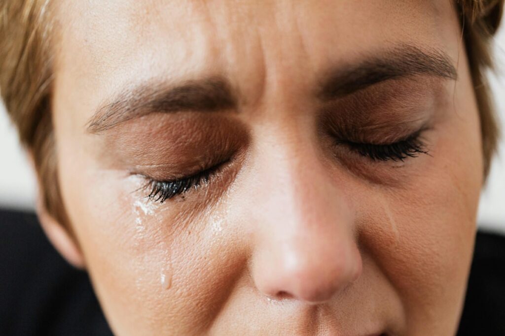 A view of a meth addict, who is a young woman, crying at looking at us while sitting against a wall