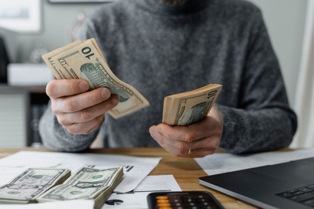 a woman sitting in her living room using a calculator and her laptop on money management for recovering addicts